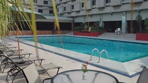 A pool area with lounge chairs and a table, surrounded by a building with multiple balconies. - Avari Lahore (Lahore)