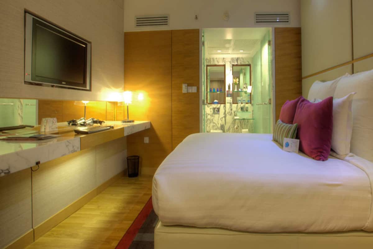 Ein Hotelzimmer mit einem Bett, einem Fernseher, einem Schreibtisch mit Lampe und einem durchgegangenen Tür erkennbaren Badezimmer.