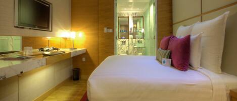 A hotel room with a bed, a TV, a desk with a lamp, and a bathroom visible through an open door.