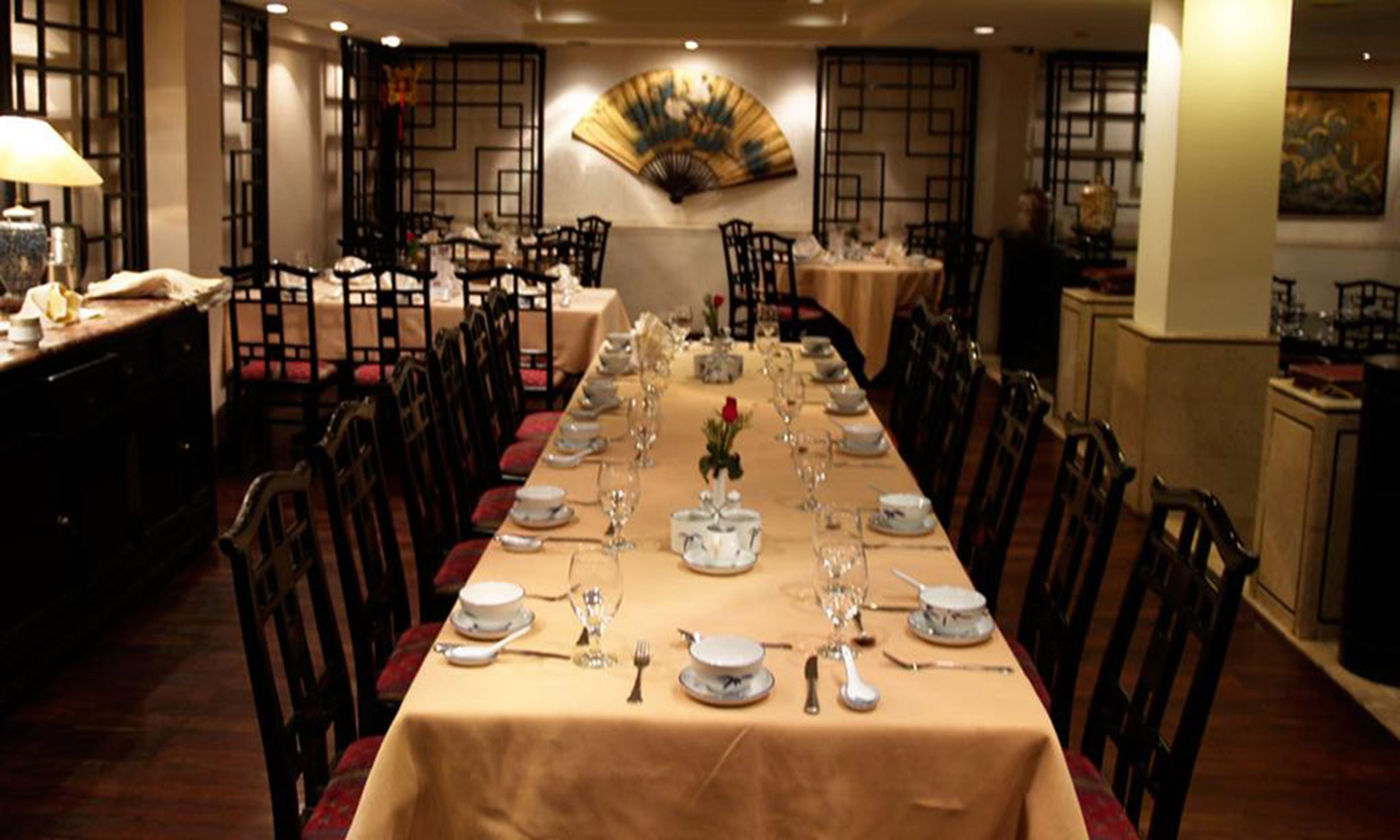 A long dining table set with white plates, glasses, and cutlery, surrounded by wooden chairs.