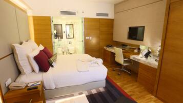 Habitación de hotel con cama, escritorio, televisor y baño visible a través de una puerta abierta.