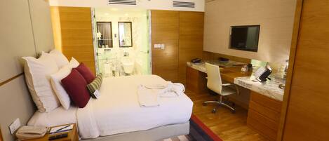 A hotel room with a bed, a desk, a TV, and a bathroom visible through an open door.