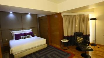 A modern hotel room with a large bed, a small side table, a chair, and a floor lamp.