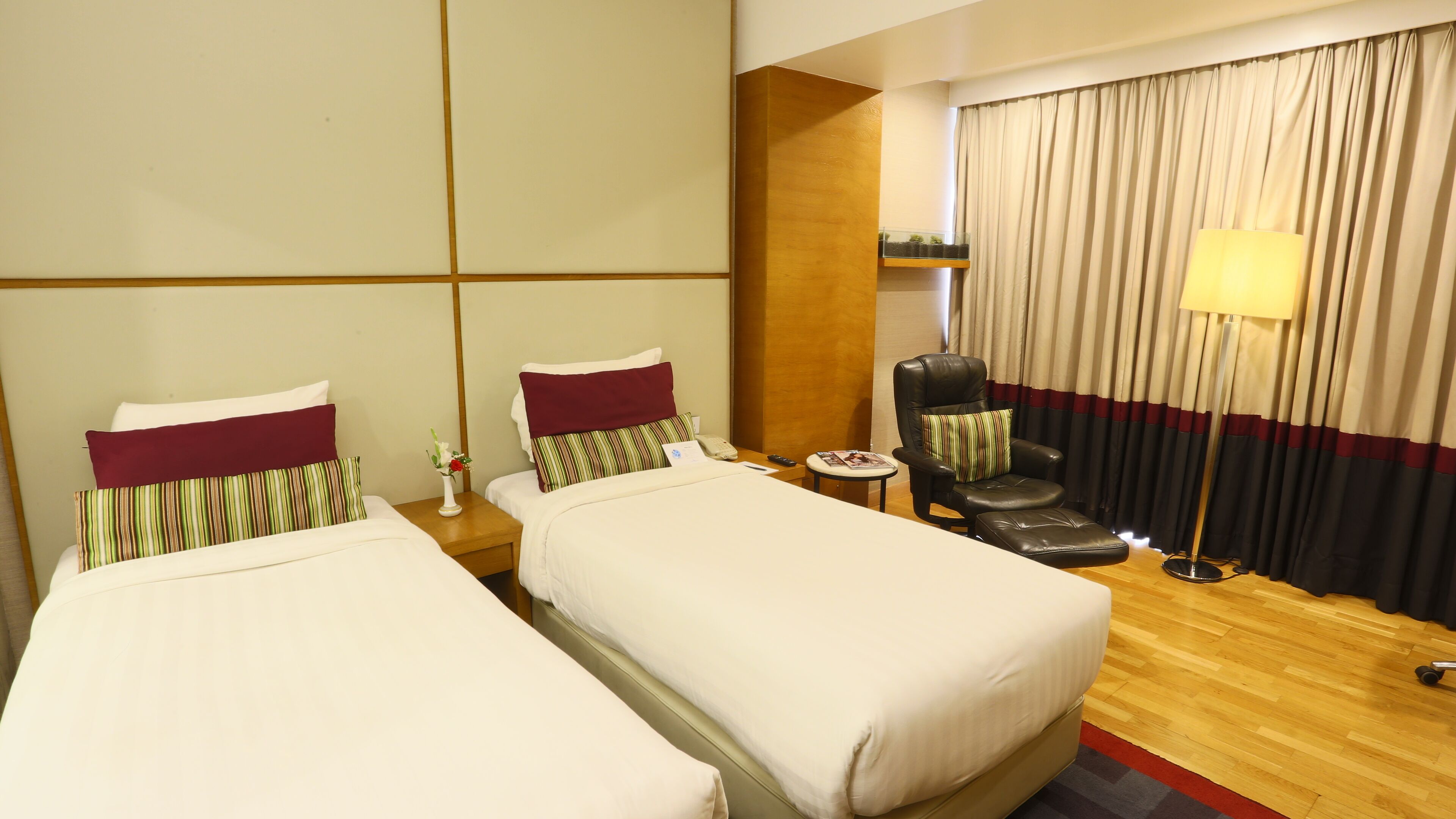 A hotel room with two single beds, a leather armchair, a small table, and a lamp.