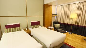 A hotel room with two single beds, a leather armchair, a small table, and a lamp.
