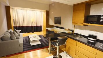 A compact living space with a sofa, a dining table with chairs, a kitchen area with a microwave, and a TV.