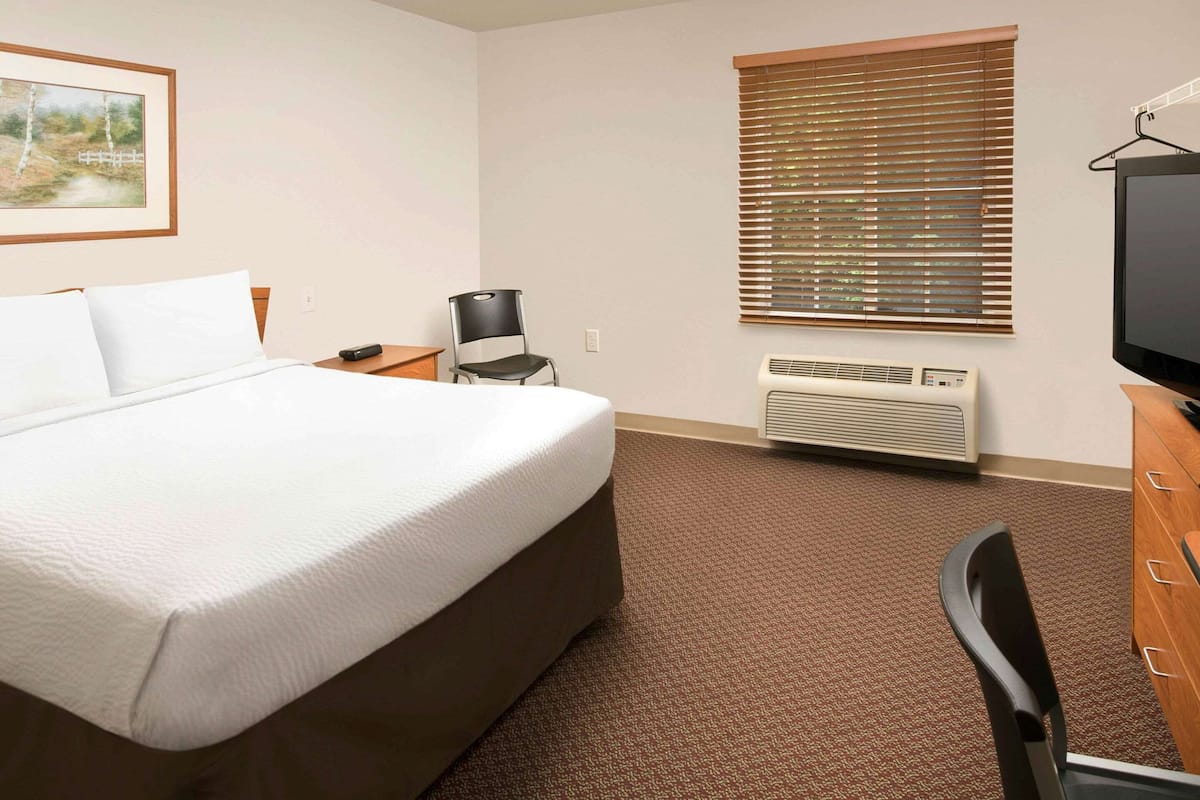 Une chambre d’hôtel avec un grand lit, un bureau, une chaise, une télévision et une fenêtre avec des stores.