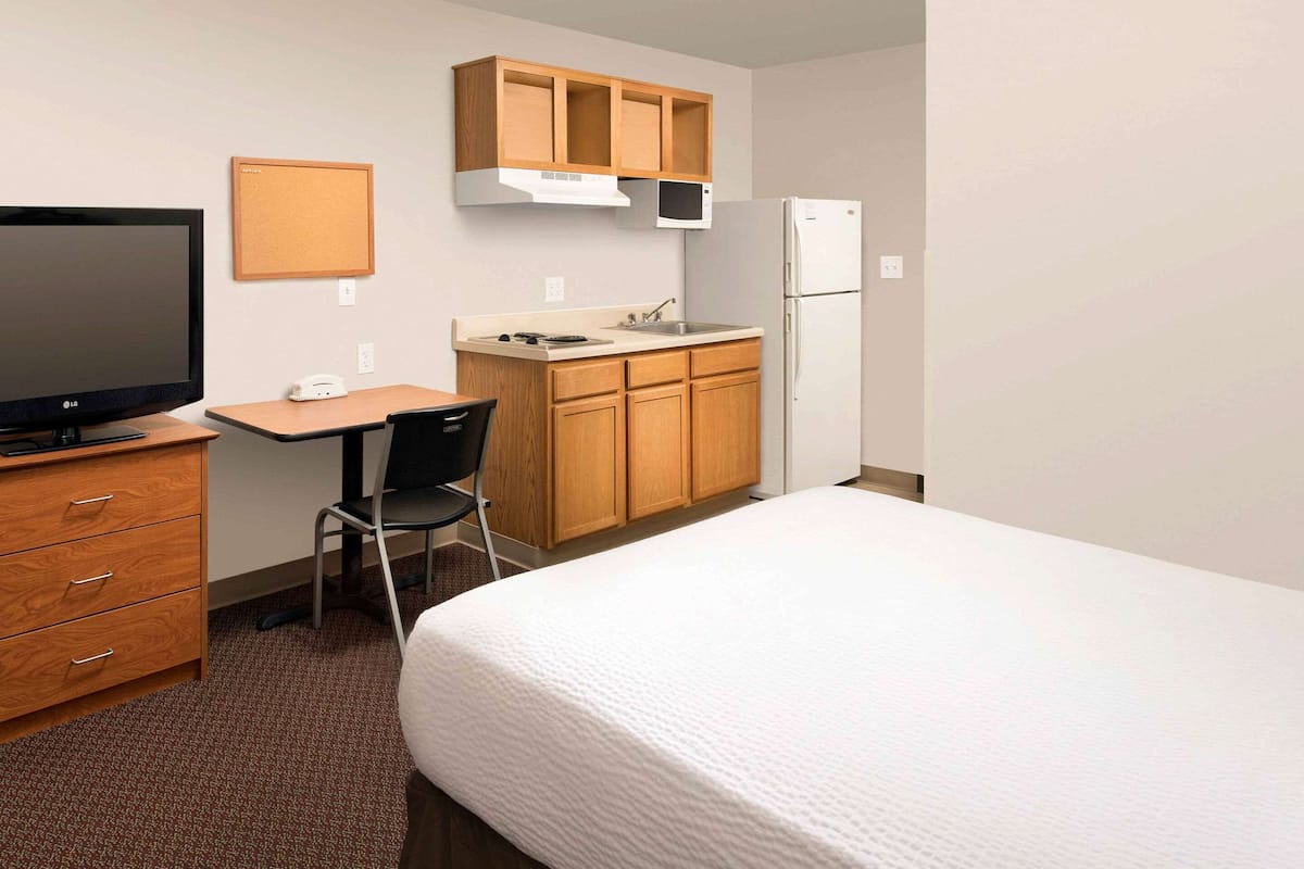 Une chambre d’hôtel compacte comprenant un lit simple, un bureau avec une chaise, une petite kitchenette équipée d’un four à micro-ondes et un téléviseur.