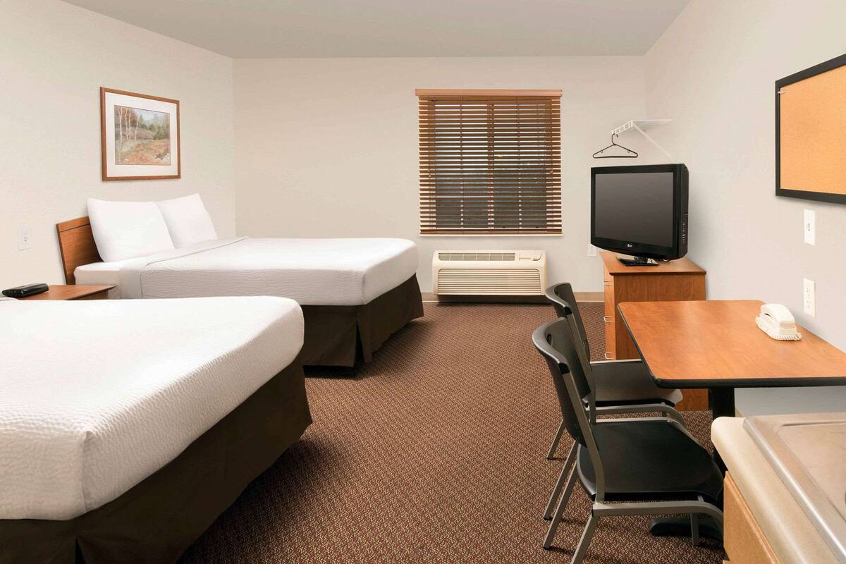Une chambre d’hôtel avec deux lits, un bureau avec une chaise, une télévision et une fenêtre avec des stores.