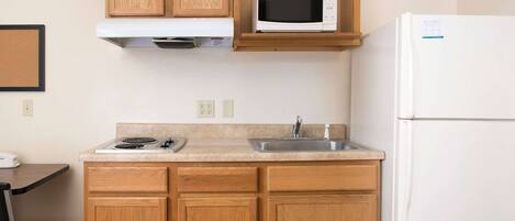 A compact kitchen with wooden cabinets, a microwave, a sink, and a refrigerator.