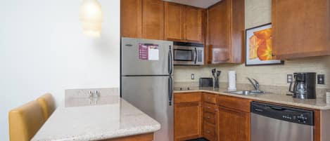 A kitchen with wooden cabinets, stainless steel appliances, a granite countertop, and a yellow chair.