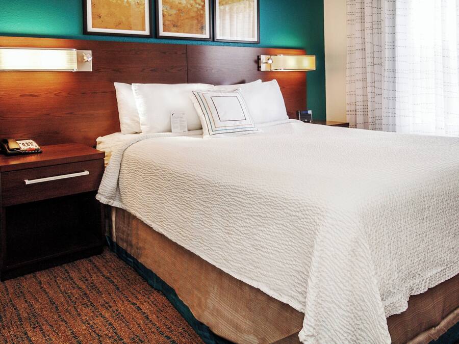 A neatly made bed with a white comforter and pillows, a wooden headboard, bedside lamps, and a telephone on a nightstand.
