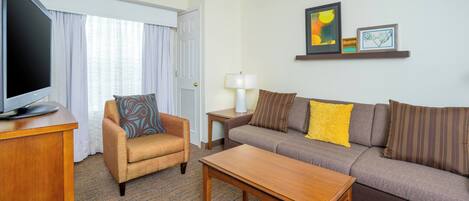 Una habitación de hotel con televisión, sofá, sillón, mesita de centro y lámpara.