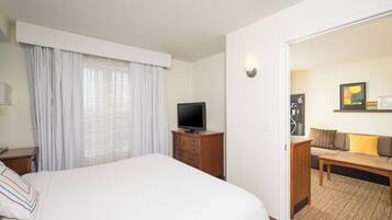 A hotel room with a bed, a television on a wooden cabinet, a sofa with cushions, and a carpeted floor.