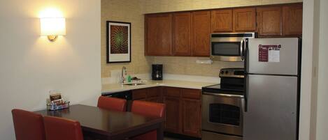 A compact kitchen with wooden cabinets, a stainless steel refrigerator, a microwave, and a coffee maker.
