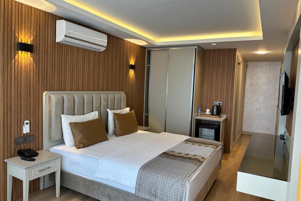Habitación de hotel moderna con una cama grande, mesitas de noche, unidad de aire acondicionado, televisión y armario.