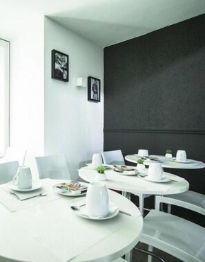 A modern dining area with white tables and chairs, black walls, and framed artwork. - Hotel Schtak (Cannes)