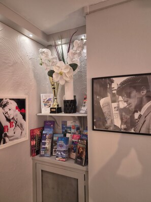 A wall with a shelf displaying books, a framed photograph, and a vase with white flowers. - Hotel Schtak (Cannes)