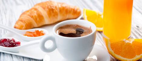 A breakfast setting with a croissant, a cup of coffee, a glass of orange juice, and a spoon with jam.
