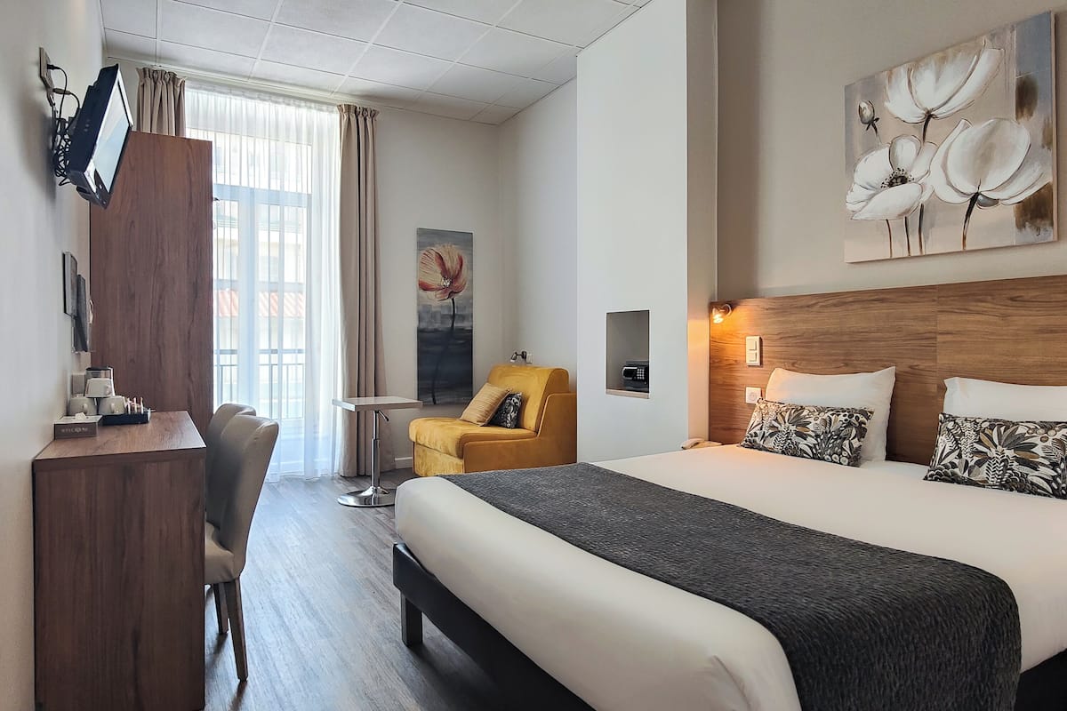 A hotel room with a bed, a desk, a chair, a TV, and artwork on the walls.