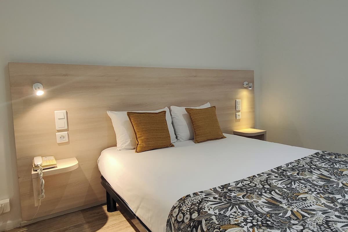 A neatly made bed with a patterned bedspread, two brown pillows, and a wooden headboard. There are bedside lamps and a telephone on the nightstand.