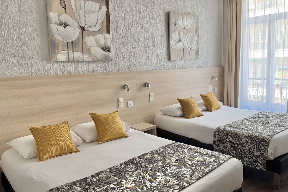 A hotel room with two beds, a wooden headboard, a patterned bedspread, and artwork on the wall.