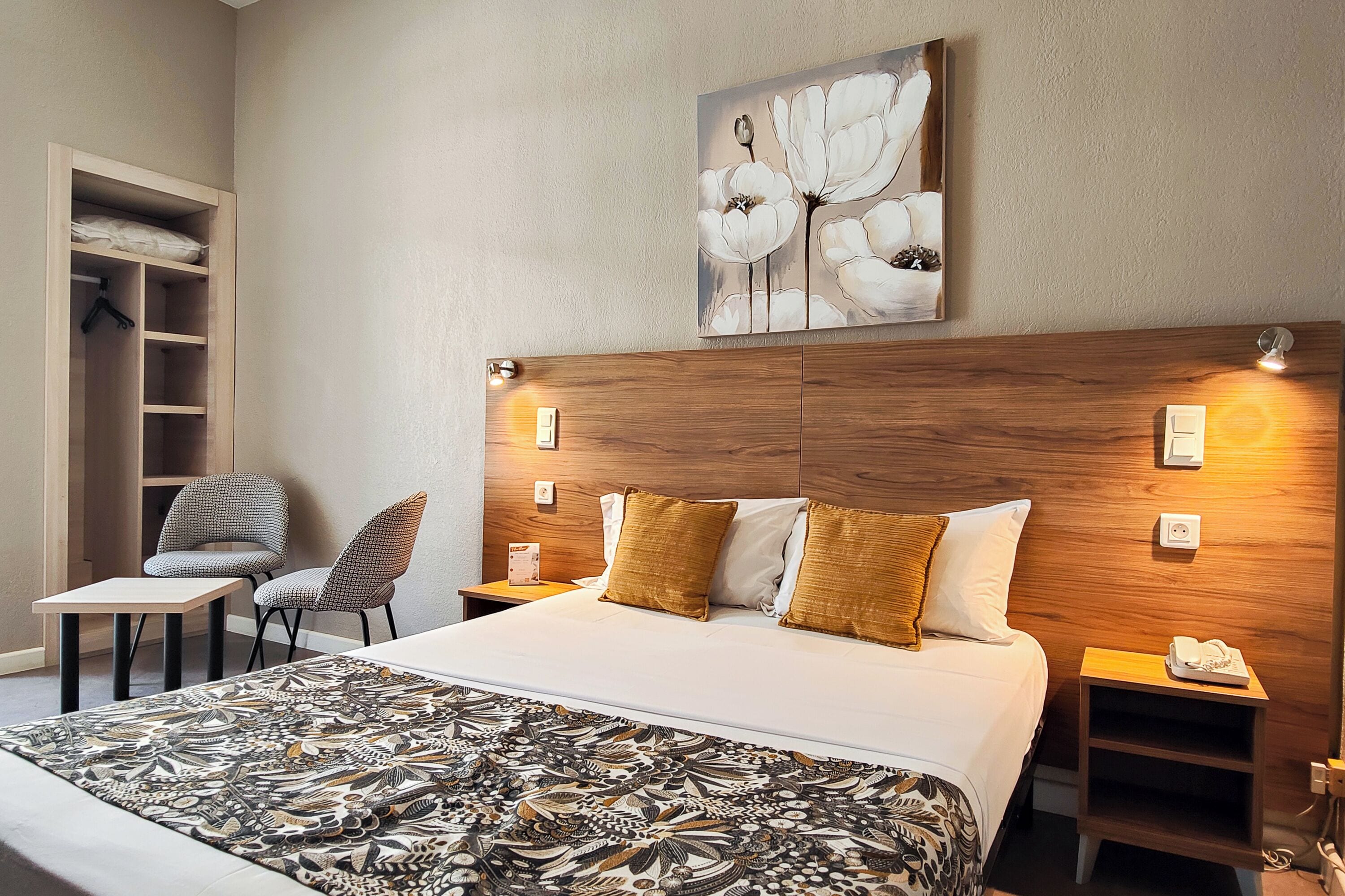 A hotel room with a bed, a chair, a small table, a wardrobe, and a painting on the wall.