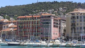 A marina with boats docked, surrounded by colorful buildings and a hillside in the background. - Hôtel Helvétique (Nice)