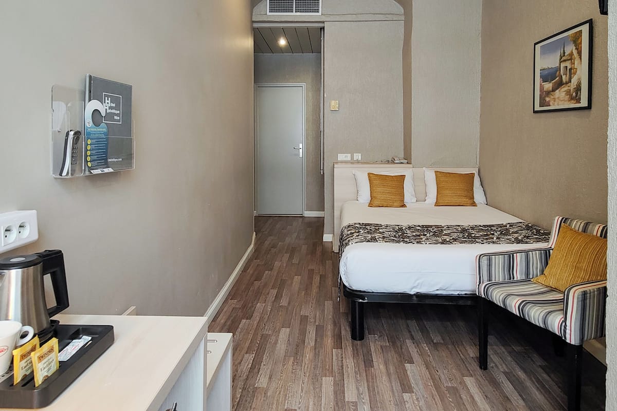 A hotel room with a bed, a sofa, a coffee maker, a phone, and a picture on the wall.
