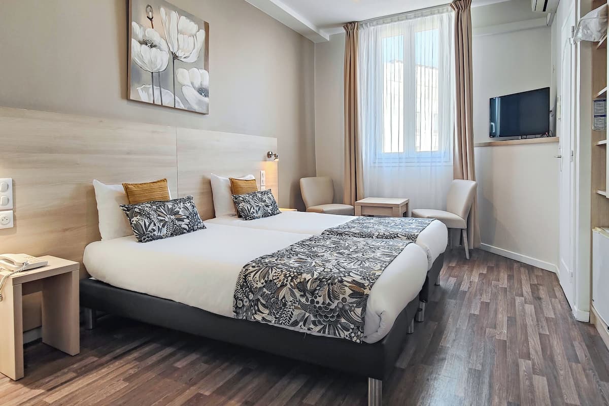 A hotel room with a large bed, bedside tables, a TV, and a window with curtains.