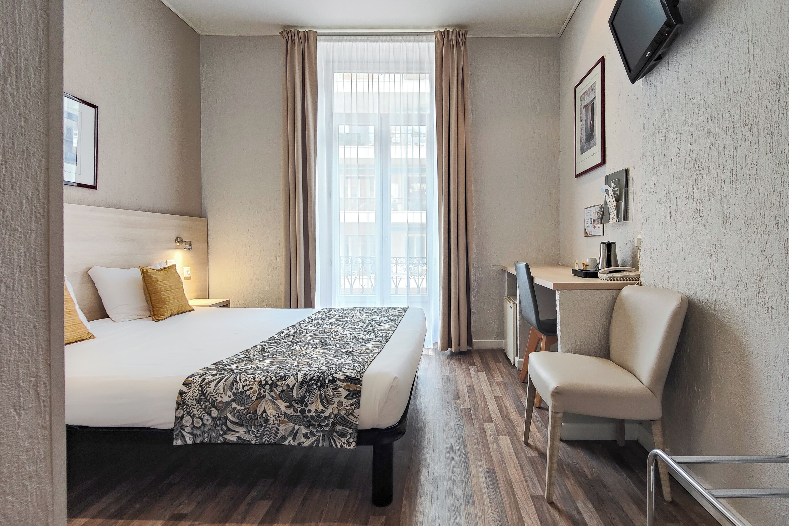 Una camera d'albergo con un letto, una scrivania, una sedia e una grande finestra.