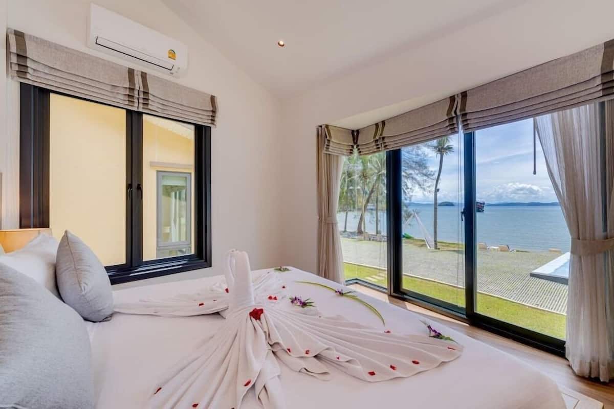 A hotel room with a bed, a view of the sea, and an air conditioning unit.
