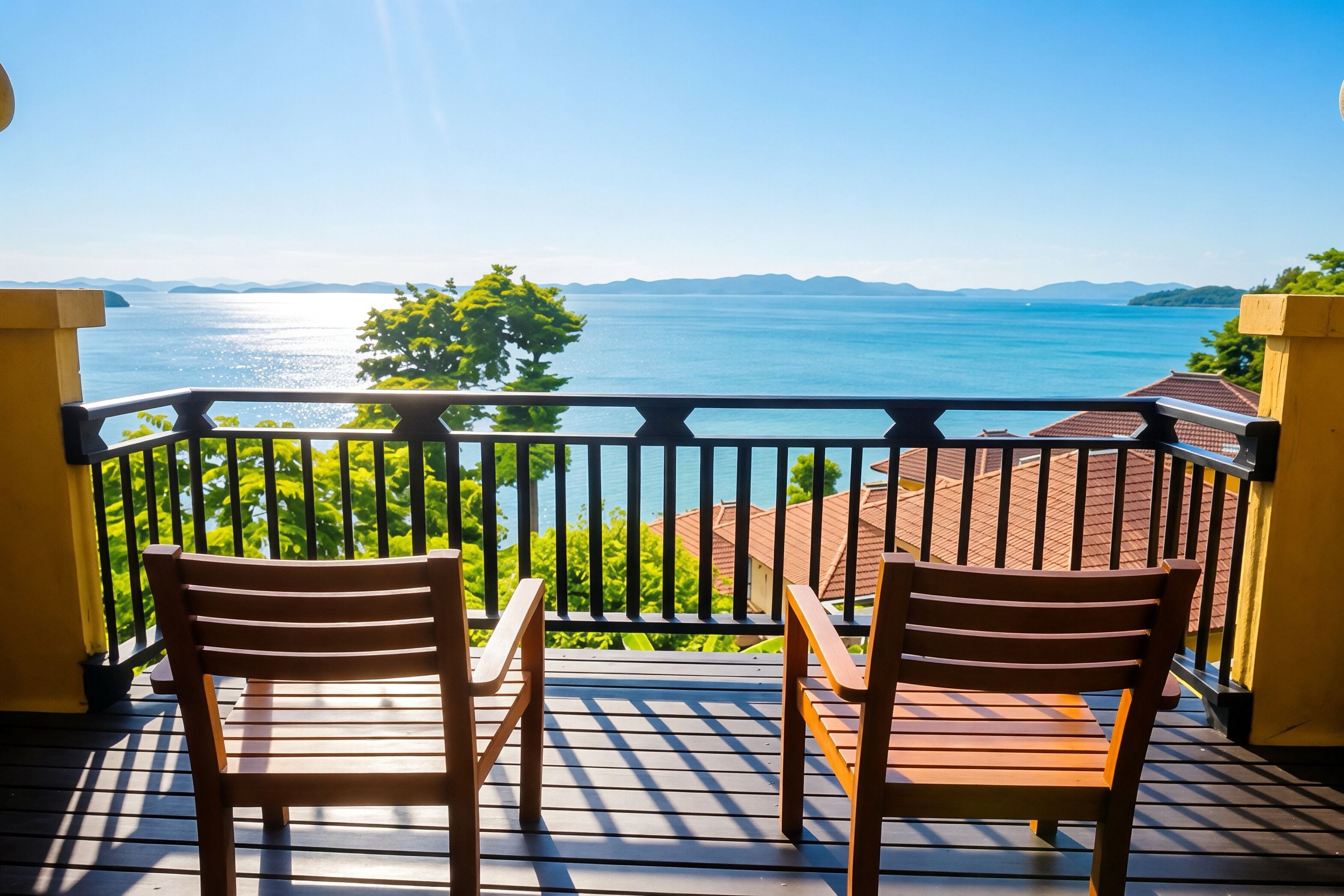 A balcony with two wooden chairs and a table, overlooking a body of water and distant mountains.