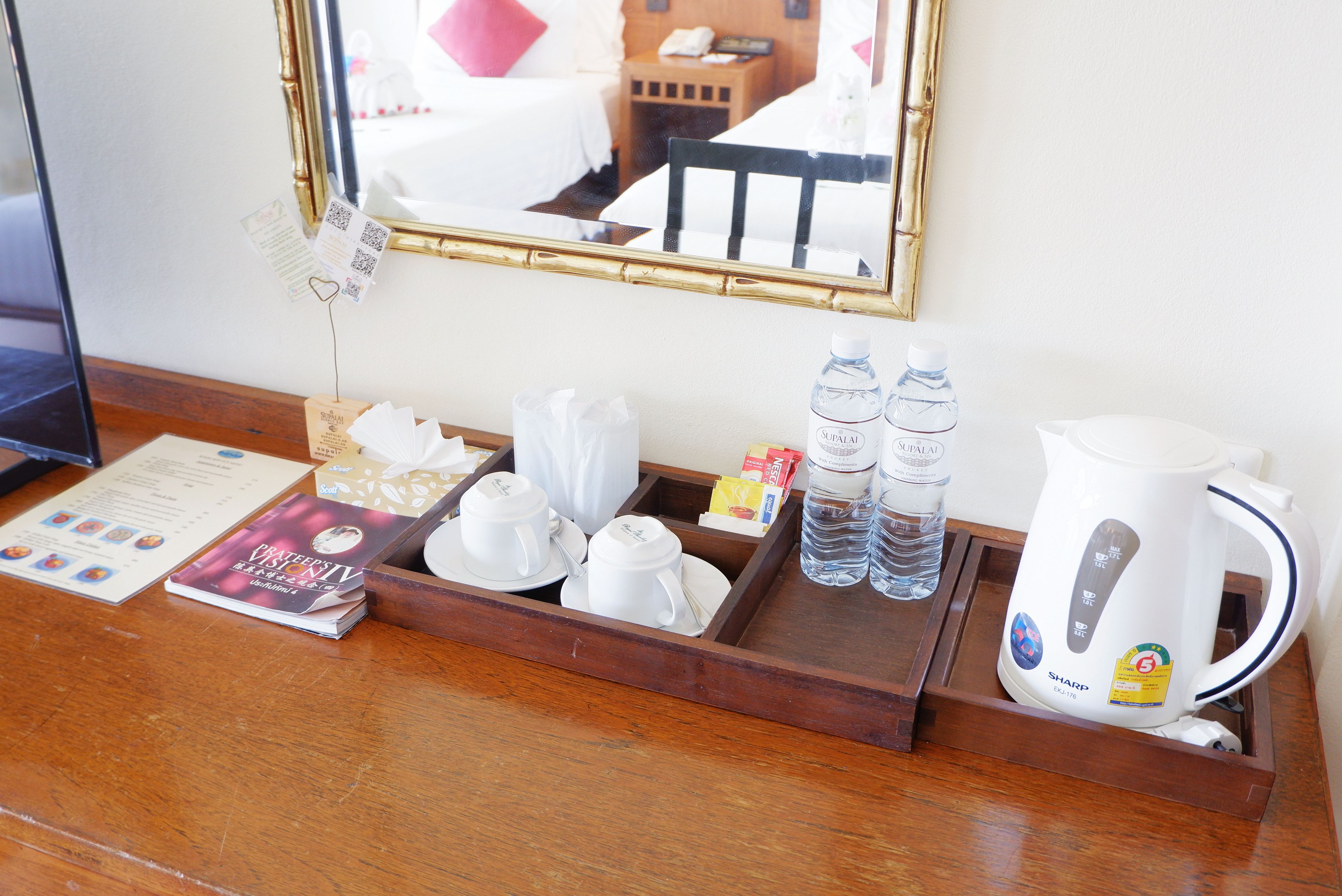 Zona de recepción de una habitación de hotel con una bandeja de madera que contiene una tetera, botellas de agua y un menú.