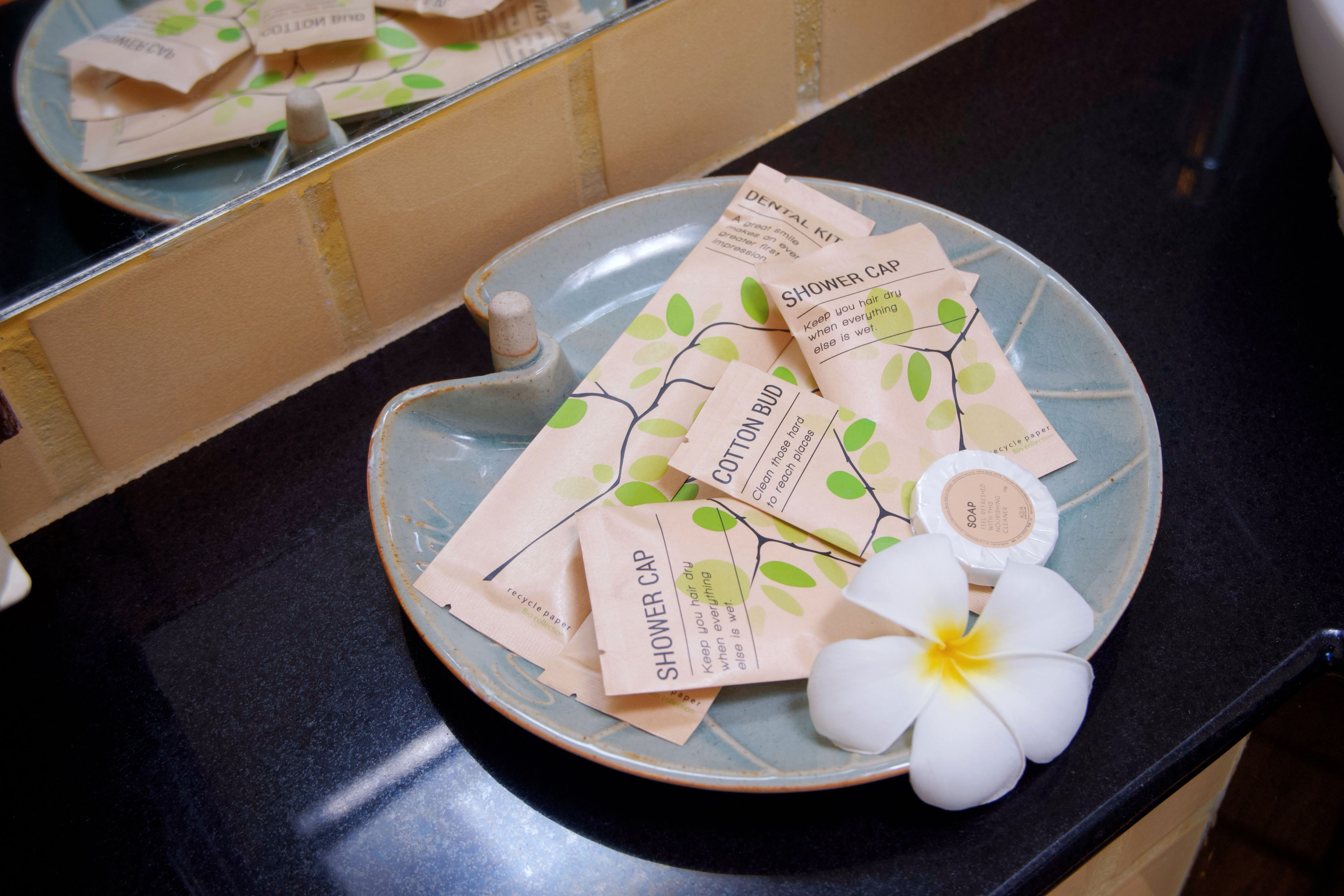 Un ripiano del bagno con un piatto in ceramica che contiene diversi copricapo per la doccia e un fiore bianco.