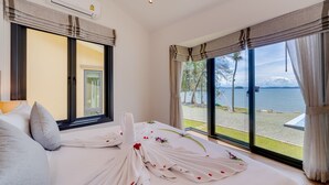 A hotel room with a large bed, a view of the sea, and a balcony with outdoor seating.