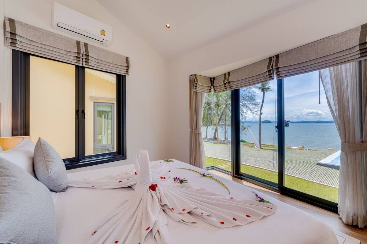 A hotel room with a large bed, a view of the sea, and a balcony with outdoor seating.