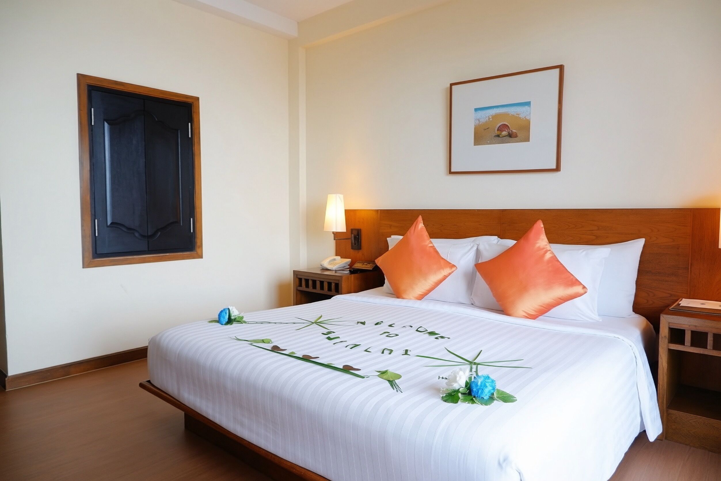 Habitación de hotel con una cama grande, una mesita de noche con lámpara, un cuadro enmarcado en la pared y una puerta con ventana.