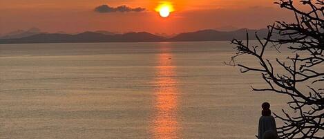 A sunset over a calm body of water with a statue in the foreground.