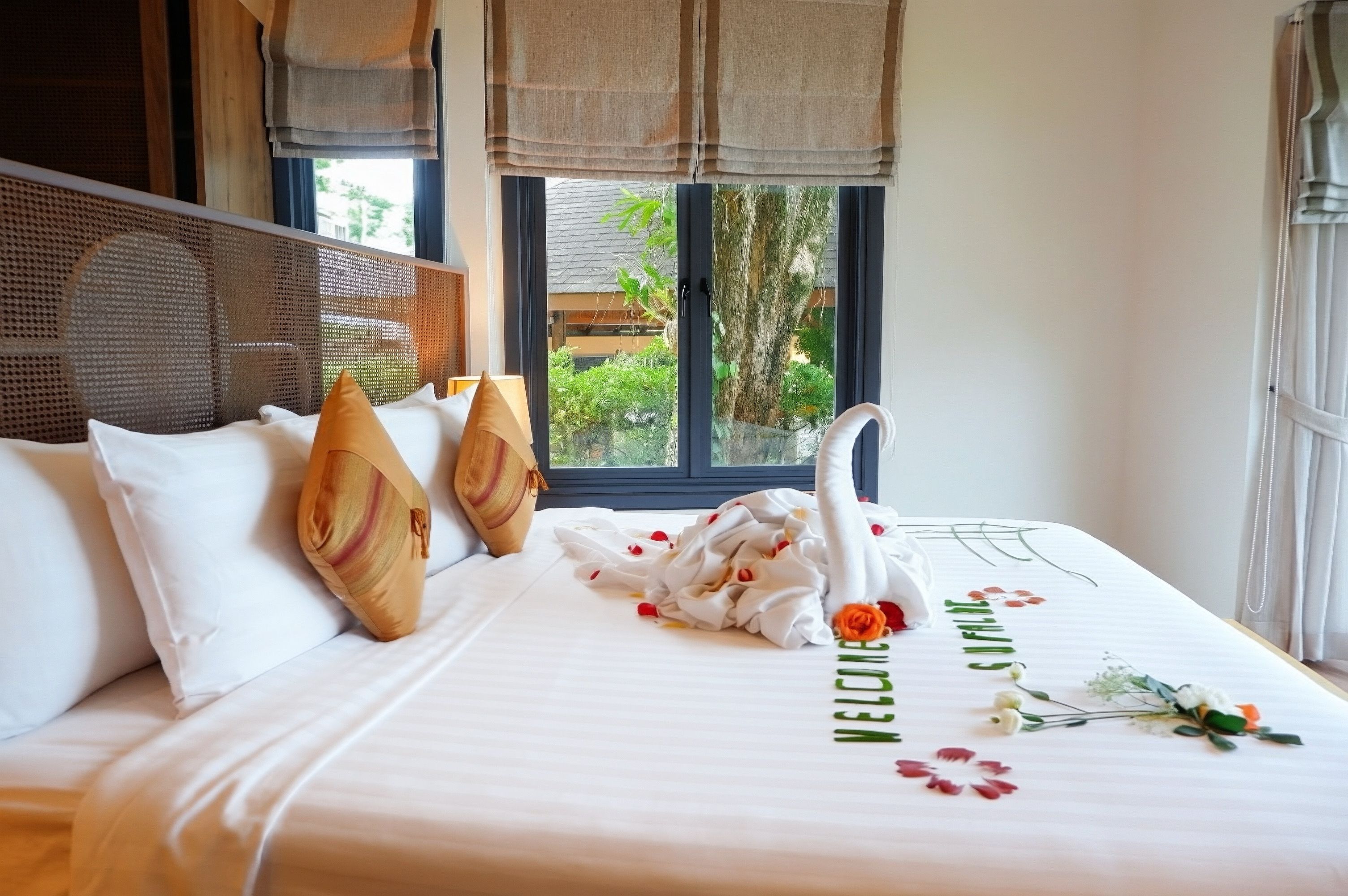 A hotel room with a bed, a window with a view of greenery, and a decorative swan on the bed.
