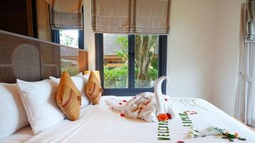 A hotel room with a bed, a window with a view of greenery, and a decorative swan on the bed.
