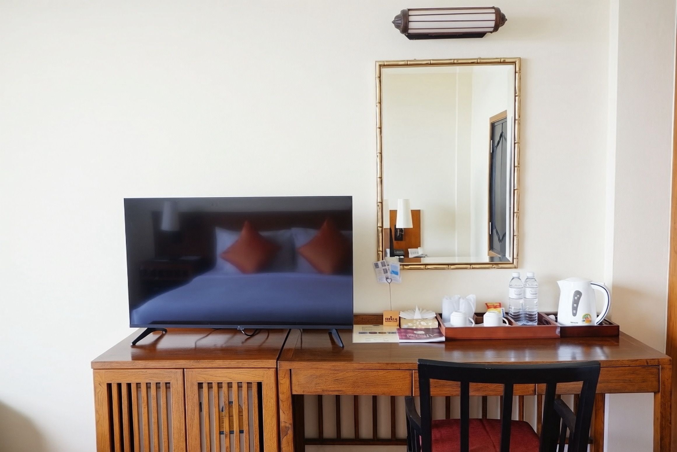 Une chambre d’hôtel avec un bureau en bois, une télévision, un miroir et un plateau contenant des articles de toilette.