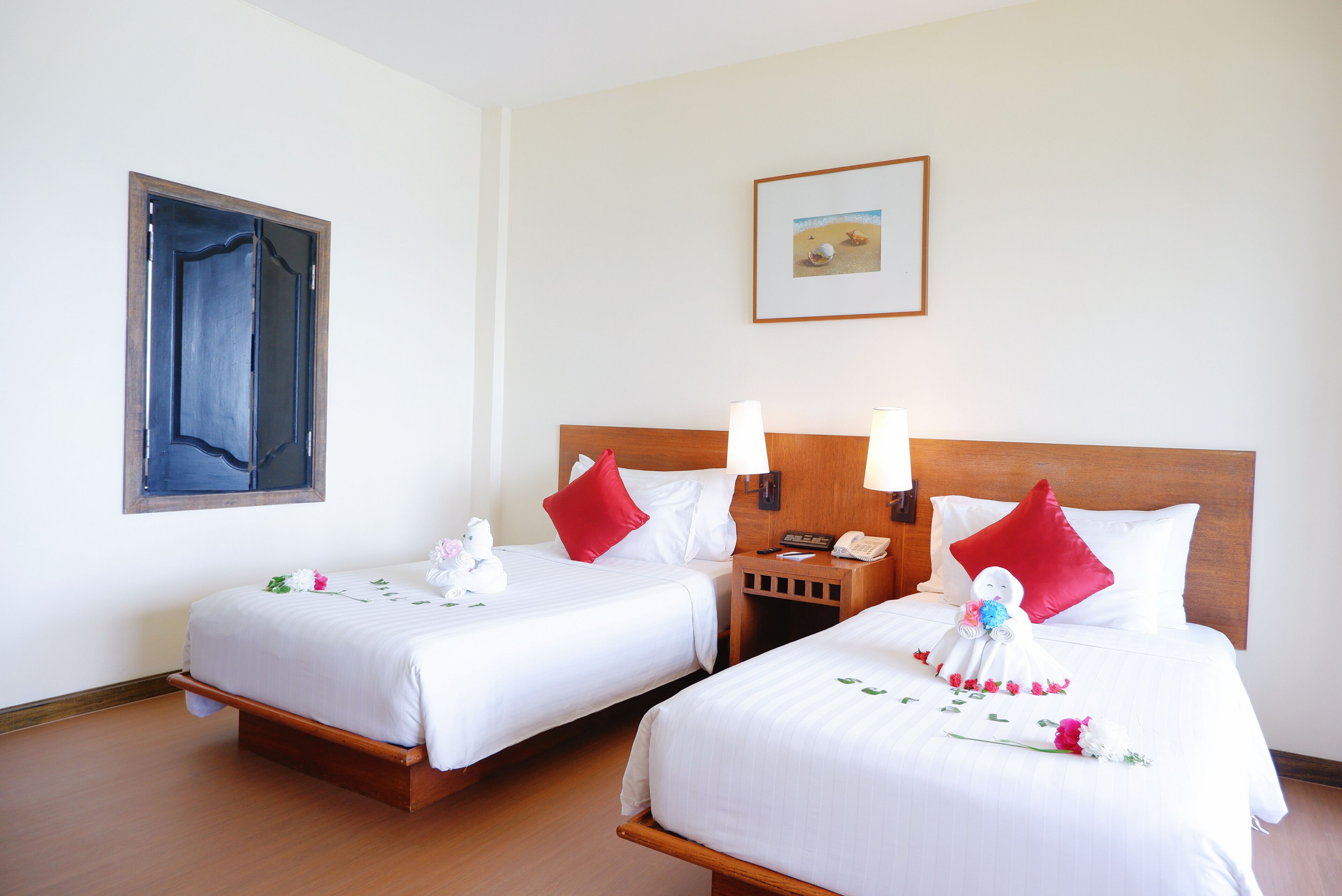 A hotel room with two beds, a wooden headboard, a nightstand with a phone, and a painting on the wall.