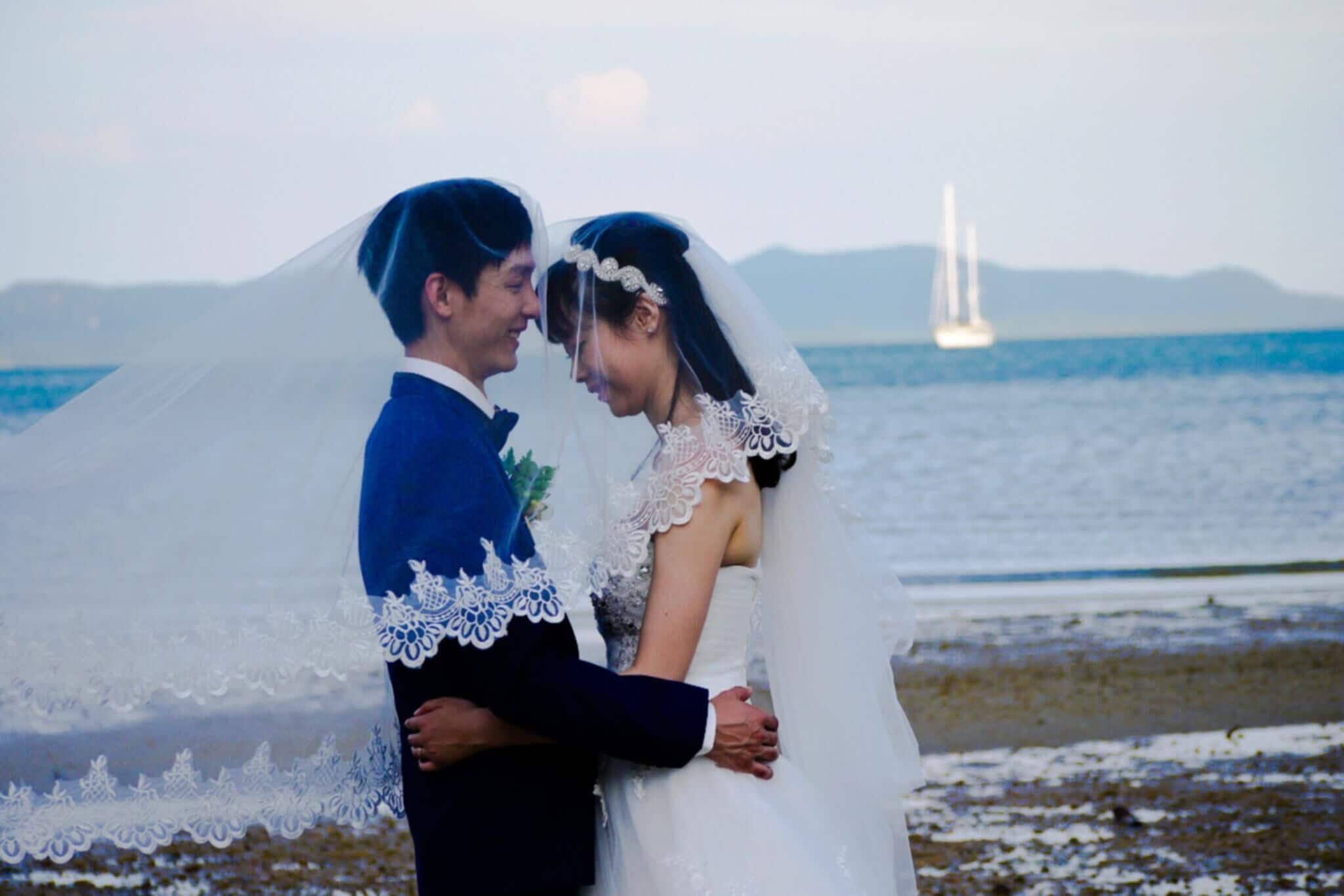 A couple embracing on a beach with a sailboat in the background.