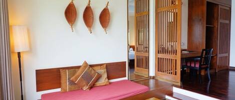 A hotel room with a wooden sofa, a small table, and a mirror reflecting a dining area.