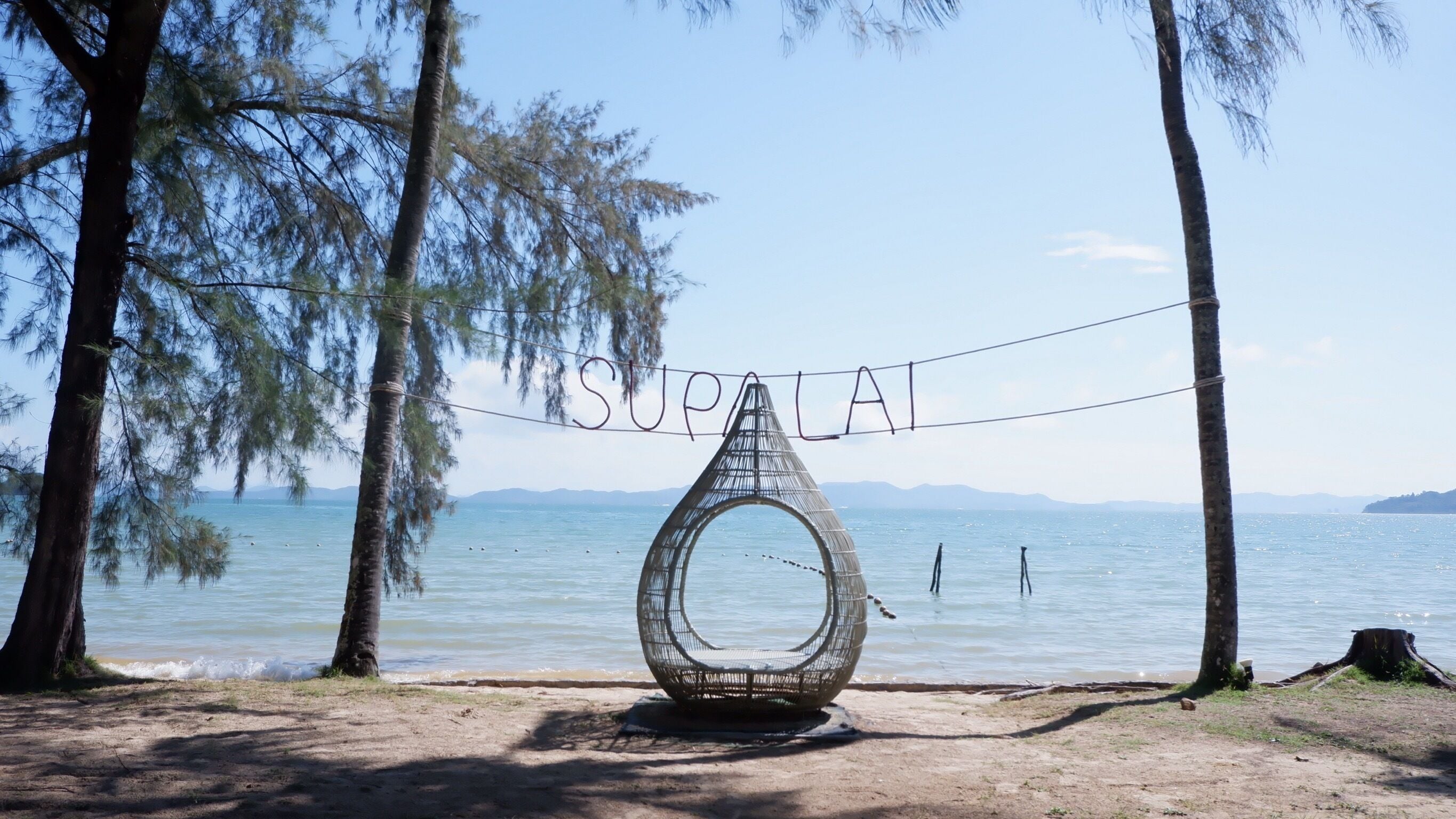 A beach with a unique spherical sculpture in the center, surrounded by trees and a clear view of the sea.