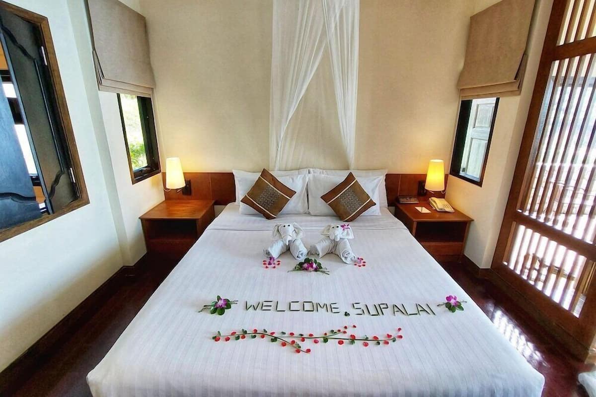 A hotel room with a large bed, two nightstands, a canopy bed, and a view through a window with blinds.
