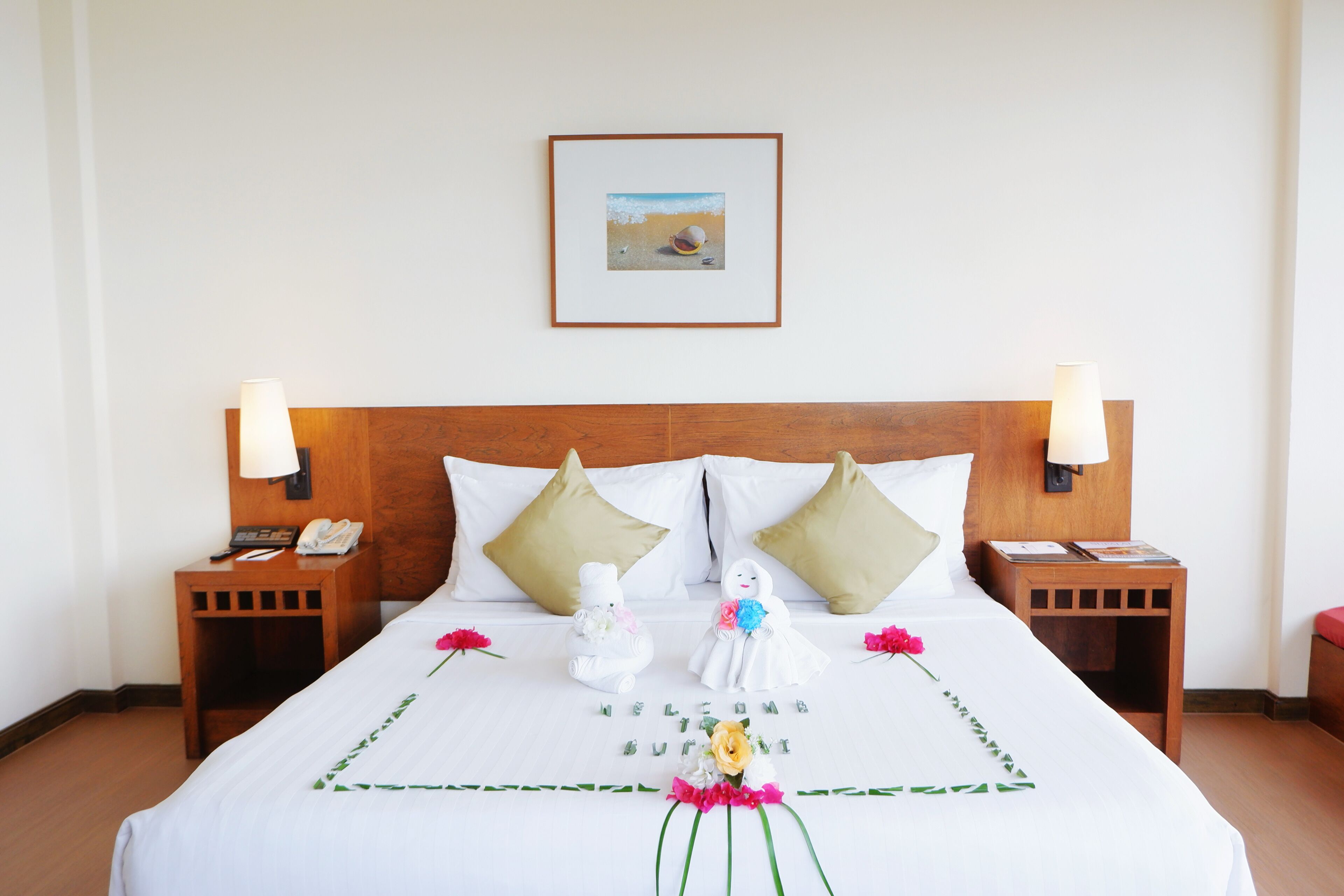 Une chambre d’hôtel avec un lit, deux tables de chevet, un tableau encadré au mur et des coussins décoratifs.