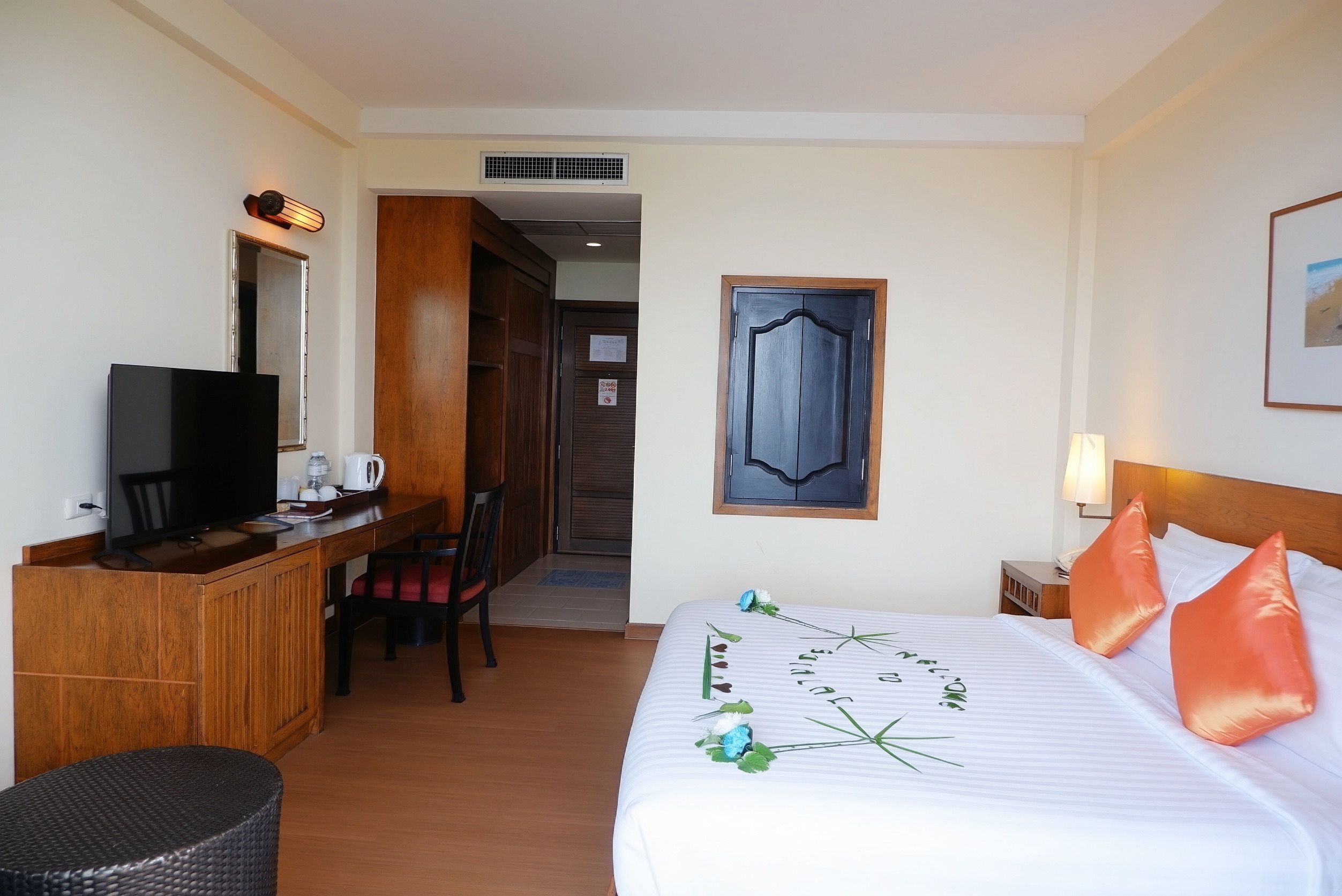 A hotel room with a bed, bedside table, lamp, desk with a chair, and a television.