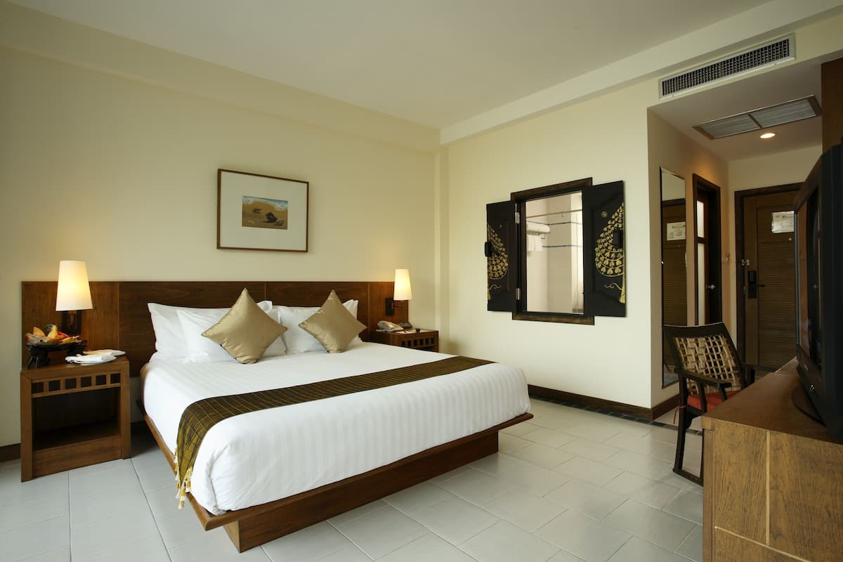 A hotel room with a large bed, two bedside tables with lamps, a wooden headboard, a framed picture on the wall, a mirror, and a desk with a chair.